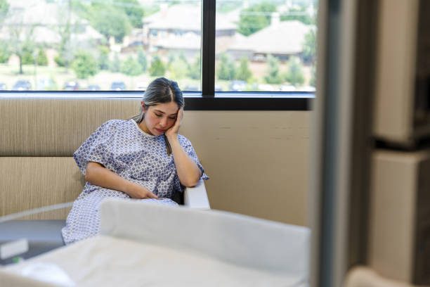 Женщина в больничном халате задумчиво сидит в больничной палате у окна.